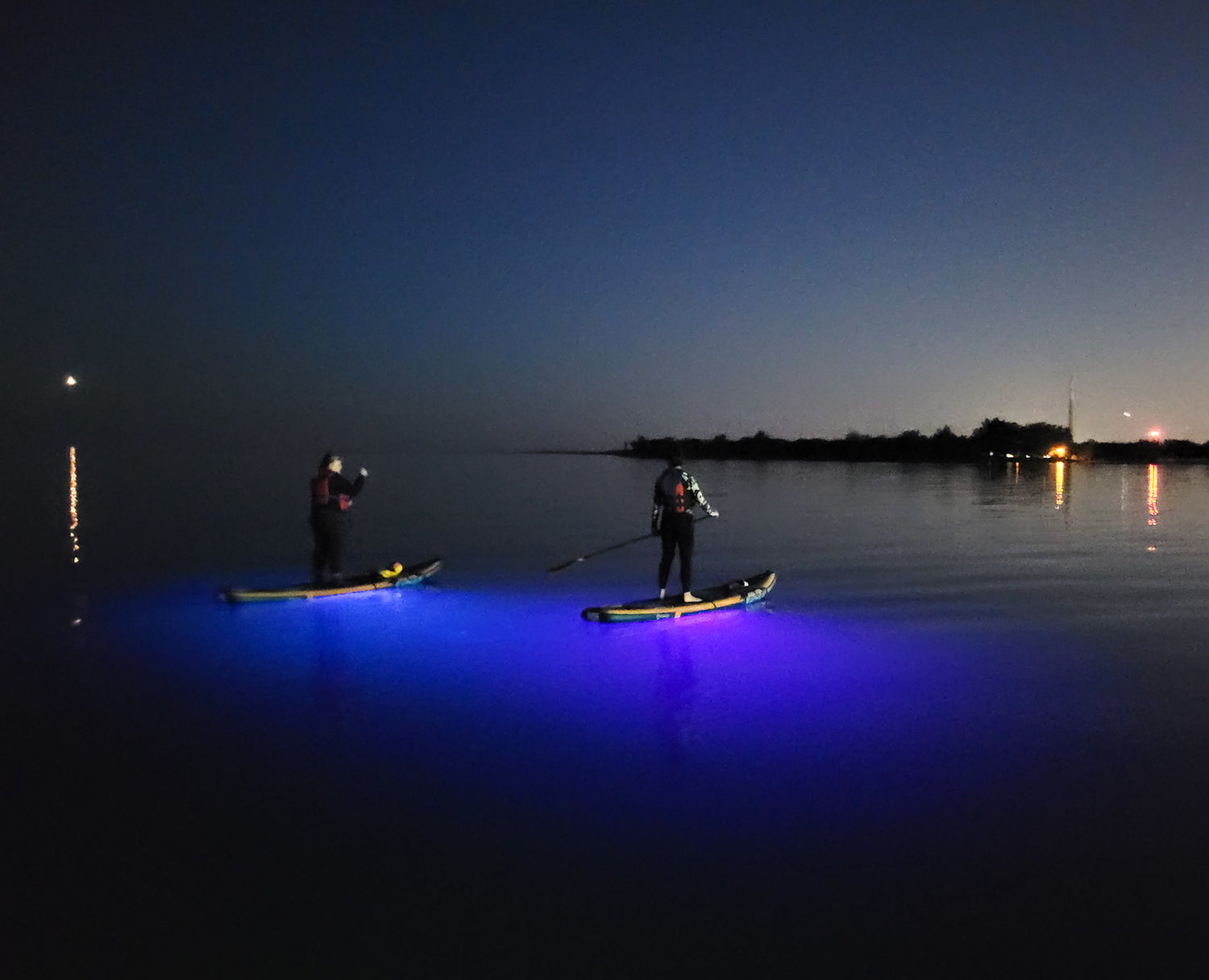 Night SUP safety with Submrg Aurora Explorer. Bright paddle board lights are illuminating the water beneath the paddleboard and creating a beautiful glow. Aurora Explorer is a safety accessory for paddleboards and kayaks.