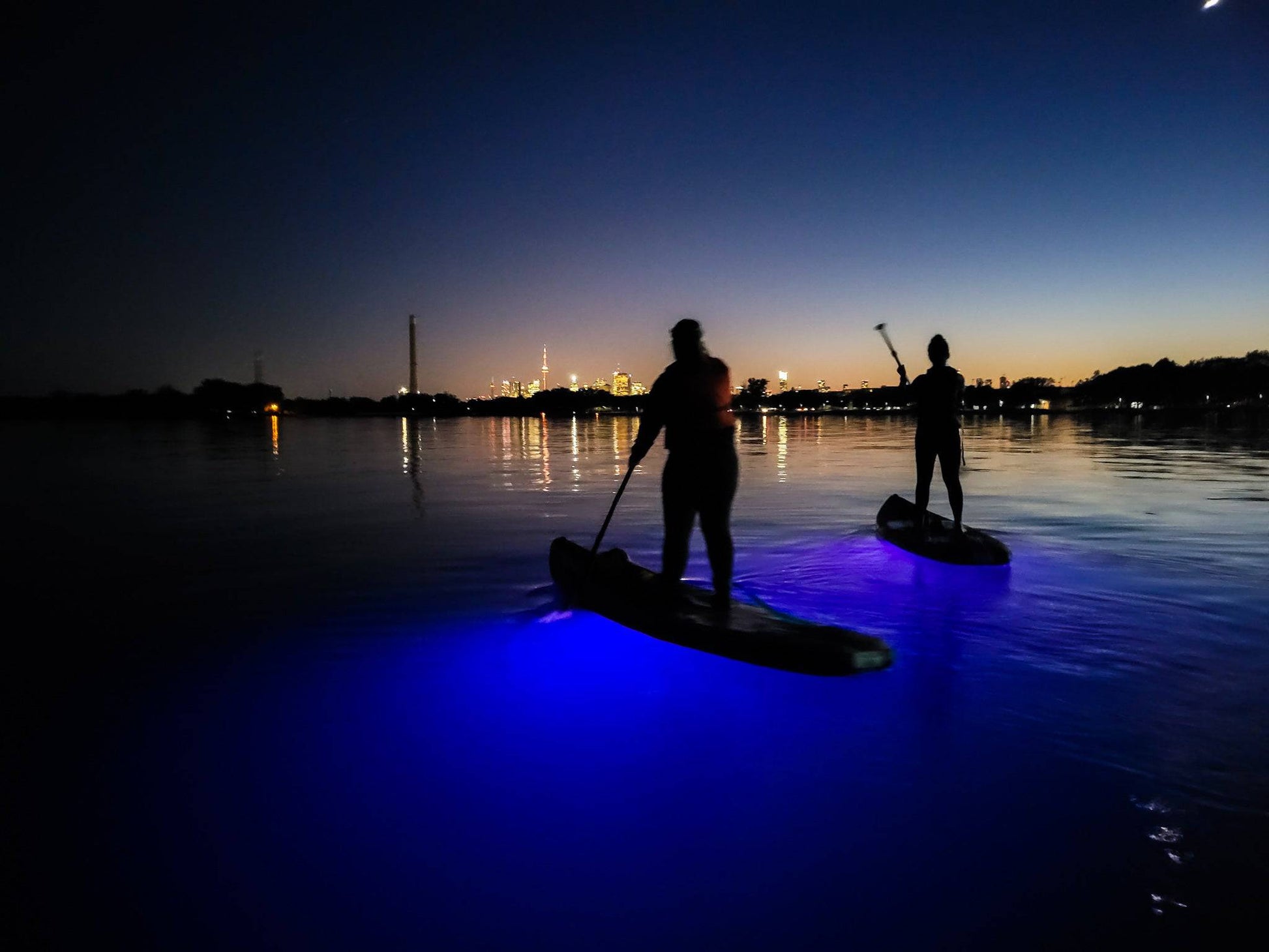 Friends enjoying the sunset while lighting up the water below their paddle boards