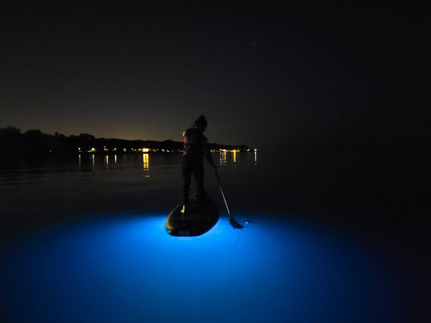 Aurora Explorer - SUBMRG. Paddle board glows in bright blue on a night SUP.