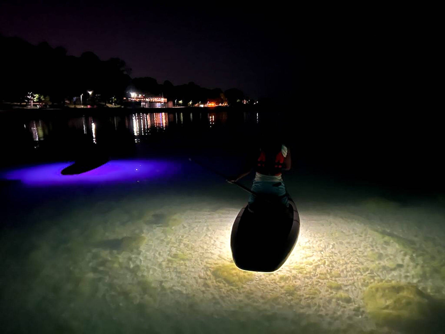 Aurora Explorer bright white light illuminates the bottom of the lake below the paddle board.